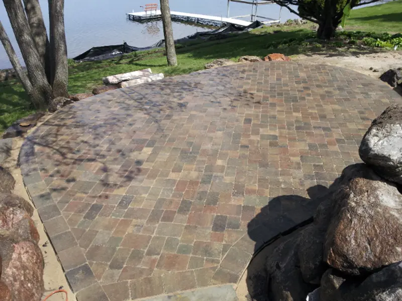 A brick patio with trees and water in the background.